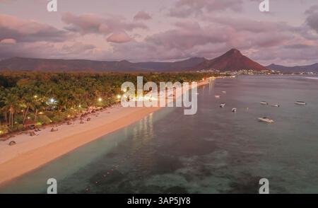 Blick aus der Vogelperspektive auf einen Strand mit Resort in Flic en FLAC mit einer Bergkette im Hintergrund und verankerten Booten. Bei Sonnenuntergang, Mauritius, Afrika. Stockfoto