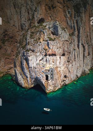 Blick aus der Vogelperspektive auf ein kleines Boot vor der touristischen Attraktion Porto Flavia mit Blick auf das Mittelmeer, Sardinien, Italien. Stockfoto