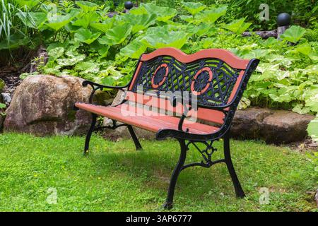 Antikes, bräunlich-orange lackiertes Holz und schwarze gusseiserne Sitzbank im Vorgarten im Frühjahr. Stockfoto