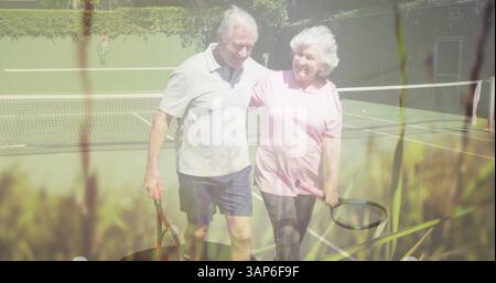 Zusammengesetzt aus glücklichem kaukasischem Seniorenpaar, das nach Tennis umgeht, mit Gras und Natur Stockfoto