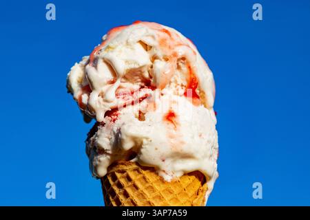Eine Schaufel Eis in einem Waffelkegel mit einer rosa Sauce drauf. Das Eis ist weiß und die Sauce rot. Der Kegel sitzt auf blauem Hintergrund Stockfoto