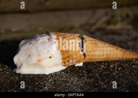 Ein halb gegessen Eiskegel, aus dem eine weiße Flüssigkeit tropft. Der Kegel befindet sich auf einer Felsoberfläche Stockfoto