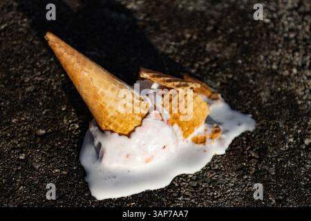 Ein halb gegessen Eiskegel, aus dem eine weiße Flüssigkeit tropft. Der Kegel befindet sich auf einer Felsoberfläche Stockfoto