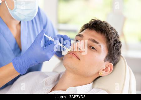 Professionelle Kosmetikerin Hände in Handschuhen, die eine Lippenverbesserung bei männlichen Klienten durchführen und Lippenfüller injizieren Stockfoto