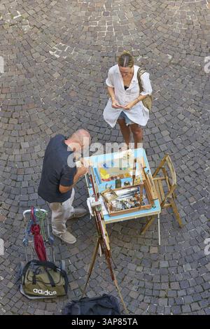 Ein Urlauber in Malcesine kauft ein gemaltes Bild von einem Straßenkünstler als Souvenir Stockfoto