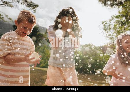 Eine Gruppe glücklicher Kinder genießt einen verspielten Moment inmitten von Wasserspritzern in einer sonnigen Umgebung im Freien, die die Freude und den Spaß der Kindheit einfängt Stockfoto