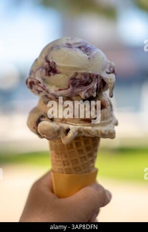 Hand hält Blaubeere und Schokoladeneis, Eis mit Waffelkegel, auf verschwommenem Hintergrund des Sees. Stockfoto