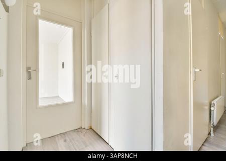 Ein heller und luftiger Flur mit einer weißen Tür mit Glaspaneel, die zu zwei geschlossenen Türen führt, die einer sauberen und modernen Ästhetik entgegenstehen. Stockfoto