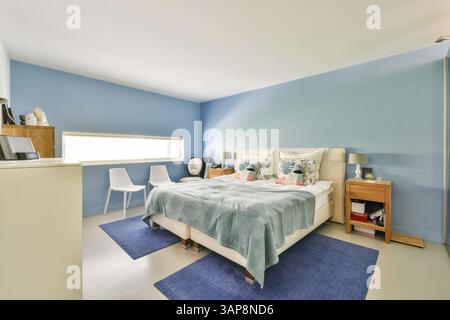 Ein wunderschön gestaltetes, modernes Schlafzimmer mit sanften blauen Wänden, gemütlichem Bettzeug und stilvollen Möbeln, die eine friedliche Atmosphäre schaffen. Stockfoto