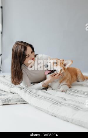 Eine fröhliche Frau genießt einen freudigen Moment mit ihrem verspielten Corgi, während sie auf einer farbenfrohen Decke sitzt, die das entzückende Bonbon wunderschön hervorhebt Stockfoto