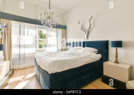Ein wunderschön gestaltetes, modernes Schlafzimmer mit einem weichen Bett, stilvollem Kronleuchter und großen Fenstern, die natürliches Licht einladen, schaffen eine ruhige Atmosphäre. Stockfoto