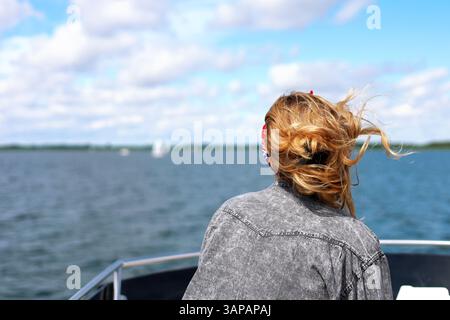 Wunderschönes blondes Mädchen im Hintergrund auf einem luxuriösen Bootsdach mit Blick in die Ferne, Haare im Wind, Segelboote im Hintergrund Stockfoto