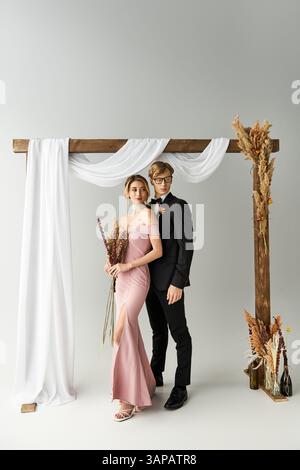 Ein glückliches Paar unter einem dekorativen Bogen, das seine elegante Frühlingshochzeit feiert. Stockfoto