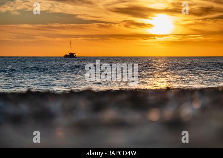 Ruhiger Sonnenuntergang mit Segelboot am Horizont, warmes goldenes Leuchten Stockfoto