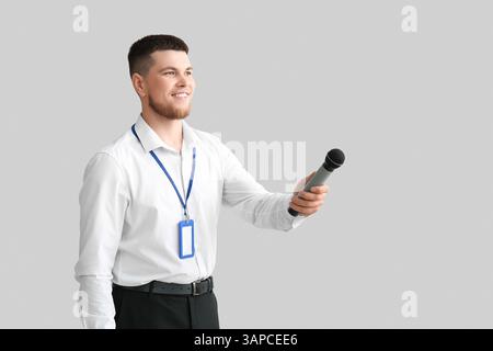Männlicher Reporter mit Mikrofon und leerem Namensschild, der ein Interview auf grauem Hintergrund macht Stockfoto