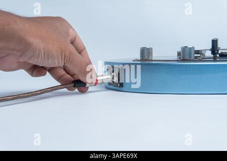 Nahaufnahme einer Hand, die ein Audiokabel in den Körper einer blauen elektrischen Gitarre steckt. Isoliert auf weißem Hintergrund. Stockfoto