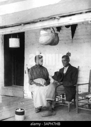 Eine afroamerikanische Frau und ein Mann sitzen zusammen auf einer Veranda. Das Foto fängt sie in einem Moment der Ruhe ein und bietet einen Einblick in das tägliche Leben afroamerikanischer Individuen während des frühen 20. Jahrhunderts. Das Umfeld und die Zusammensetzung deuten auf ein Gefühl von Gemeinschaft und Resilienz hin. Stockfoto