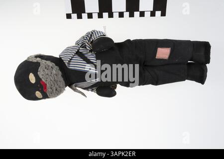 Diese männliche Puppe aus schwarzem Stoff, gekleidet mit einem schwarzen Overall und einem gestreiften Hemd, wurde Margaret Mary Moore geschenkt, als sie fünf Jahre alt war. Die Puppe repräsentiert ein Stück Kindheitsgeschichte und die materielle Kultur der Mitte des 20. Jahrhunderts und spiegelt die beliebten Spielzeuge und Geschenke der Zeit wider. Stockfoto