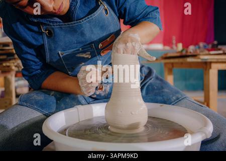 Nahaufnahme der Hände einer Latina, die in ihrer Werkstatt ein Keramikstück Formen. Das Bild erfasst Aufwand, Fokus und handgefertigte Details. Stockfoto