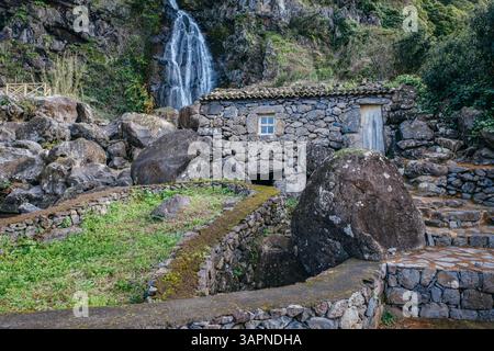 Eine charmante Ruine aus Stein liegt eingebettet zwischen Felsen in der Nähe eines wunderschönen Wasserfalls in Sao Jorge, Azoren, Portugal. Eine malerische Szene Stockfoto