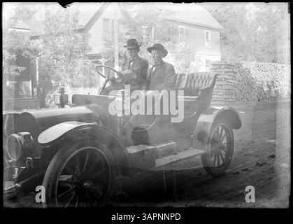 Lee Moorhouse fotografiert eine Autoparade in Pendleton, Oregon, auf der zwei Männer in einem Auto vor einem Haus gezeigt werden, die das Ereignis des frühen 20. Jahrhunderts dokumentieren. Stockfoto
