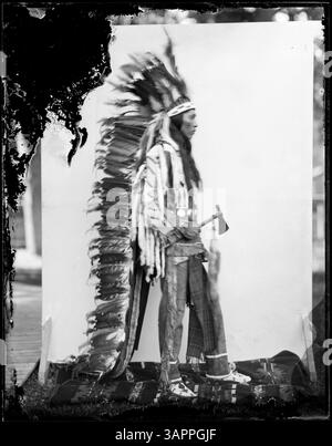 Foto eines Stammesmannes in Insignien, der ein Beil hält. Dieses Bild wurde von Lee Moorhouse aufgenommen und ist Teil der Sammlung der Bibliotheken der University of Oregon, die einen Ureinwohner in traditioneller Kleidung darstellen. Stockfoto
