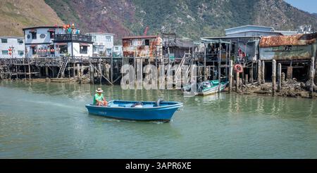 Hongkong. China- 02.27.2025. Ein kleines Boot, das auf dem Wasserweg des Fischerdorfes Tai O segelt, mit Häusern auf Stelzen am Ufer. Stockfoto