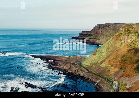 Moody Aerial View of Giant’s Causeway mit Wellen, die in die Felsen stürzen und Menschen herumlaufen Stockfoto