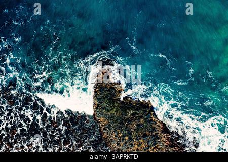 Von oben nach unten mit der Drohne sehen Sie die schäumenden Wellen, die entlang der Küste auf die Felsen treffen Stockfoto