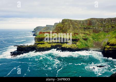 Dramatische Luft der Giant’s Causeway Cliffs mit abstürzenden blauen Wellen während eines bewölkten Tages Stockfoto