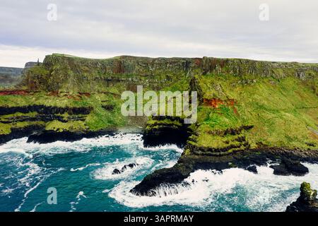 Dramatische Luft der Giant’s Causeway Cliffs mit abstürzenden blauen Wellen während eines bewölkten Tages Stockfoto