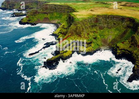 Dramatische Luft der Giant’s Causeway Cliffs mit abstürzenden blauen Wellen während eines bewölkten Tages Stockfoto