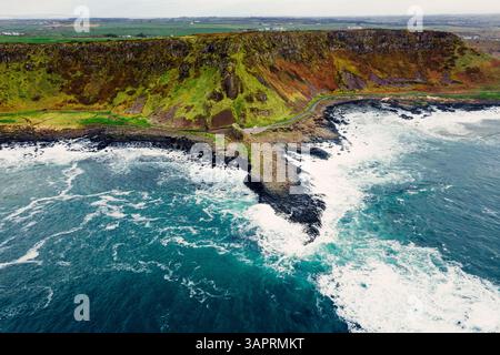 Moody Aerial View of Giant’s Causeway mit Wellen, die in die Felsen stürzen und Menschen herumlaufen Stockfoto