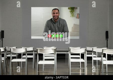 Redner, der über Online-Videochat an der Vorlesung teilnimmt. Leerer Konferenzraum mit Projektionsleinwand und Stühlen Stockfoto