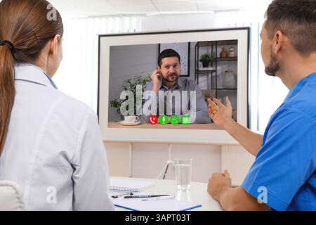 Redner, der über Online-Videochat an der Vorlesung teilnimmt. Medizinisches Personal im Konferenzraum mit Projektionsleinwand Stockfoto