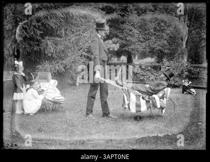 Dieses Foto von Lee Moorhouse zeigt einen Mann und einen kleinen Mann im Kostüm, mit einem Hund, der eine Pfeife im Mund hält, und zeigt die Charaktere „Mutt and Jeff“ aus der amerikanischen Unterhaltung des frühen 20. Jahrhunderts. Stockfoto