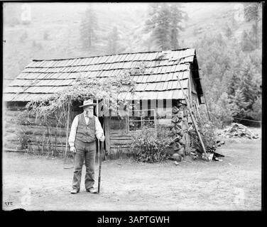 Foto von Hager Cabin in in der Nähe von Bingham Springs, mit einem Mann, der draußen ein Gewehr hält. Dieses Bild wurde von Lee Moorhouse aufgenommen und ist Teil der Sammlung der Bibliotheken der University of Oregon, die das ländliche Leben in Oregon darstellt. Stockfoto