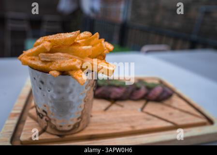 Nahaufnahme von gewürzten Pommes Frites in Metallic Cup auf Holzbrett Stockfoto