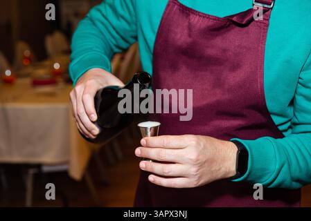 Nahaufnahme eines Barkepers, der auf einer Schürze schaumiges Bier in ein Glas bei einer gesellschaftlichen Veranstaltung oder Party gießt. Stockfoto