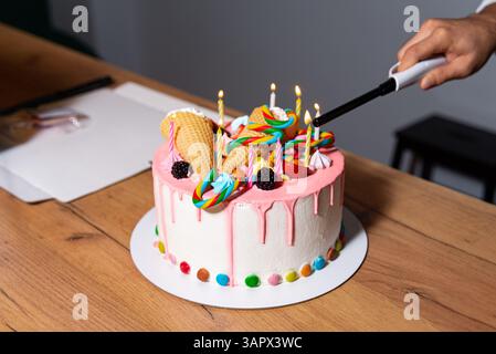 Handzünder auf lebendigem Geburtstagskuchen, dekoriert mit Süßigkeiten, Lutscher, Eiskegel und rosa Glasur. Stockfoto