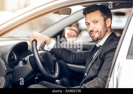 Glücklicher junger Unternehmer sitzt im Auto, fahren ins Büro Stockfoto