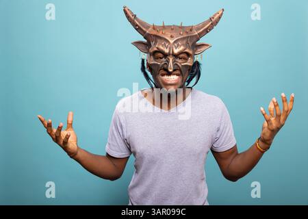 Porträt eines männlichen Models mit gruseliger Monster-Kostümmaske, posiert mit erhobenen Händen für dramatische Effekte. Nahaufnahme eines Mannes, der eine Kreaturenmaske trägt und einen gruseligen Charakter mit unheimlichen Gesichtsbewegungen verkörpert. Stockfoto