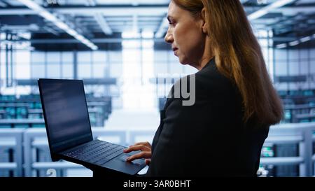 Techniker, der die Überprüfung durchführt und Daten auf Laptop mit den erforderlichen Servernhubs-Fehlerbehebungen eingibt. Nahaufnahme eines Mitarbeiters, der im Rechenzentrum arbeitet und eine erweiterte Speicherinfrastruktur zur Unterstützung von IT-Workloads bietet, Kamera B Stockfoto
