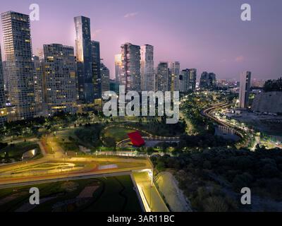 Atemberaubende Langzeitbelichtung von einer Drohne, die die beleuchtete Skyline von Santa Fe und La Mexicana Park in Mexiko-Stadt unter einem lila Abend zeigt Stockfoto