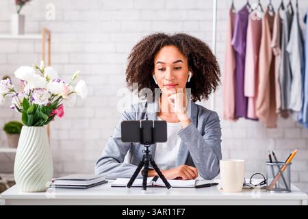 Online-Chat mit Followern während des Coronavirus-Ausbruchs. Ernsthafte aftere afroamerikanische Frau mit schnurlosen Kopfhörern schaut sich das Smartphone an und macht es Stockfoto