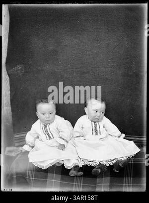 Dieses Foto zeigt Siletz-Zwillingskinder, die in traditionellen Kleidern sitzen und die kulturellen Praktiken der indianischen Kinderbetreuung repräsentieren. Stockfoto