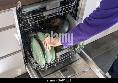 Person, die sauberes Geschirr aus einem vollen Geschirrspüler in einer Küche, England, entfernt. Konzept: Energierechnungen, Stromverbrauch in Haushalten, Wasserverbrauch, Wasserverbrauch Stockfoto