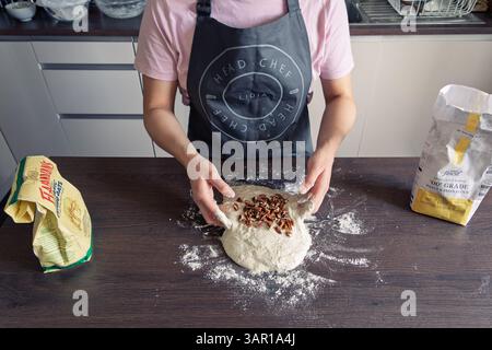 Eine Frau in ihren 30ern, die Teig küsste, eine Schürze trug und selbstgemachtes Brot mit Pekannüssen machte, Großbritannien. Konzept: Hausbacken, Komfortessen, Lifestyle Stockfoto