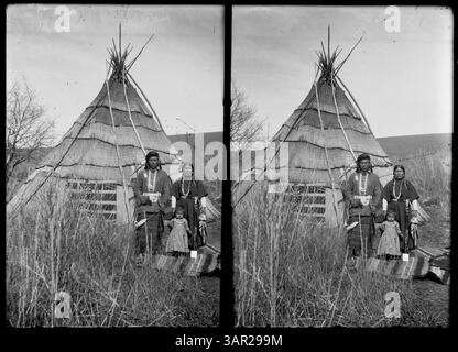 Ein Stereo-Foto, das einen Mann, eine Frau und ein Kind vor einem Tipi zeigt. Das Bild zeigt die Familie in traditioneller Kleidung und spiegelt Aspekte des Lebens der Ureinwohner und des Schutzhauses wider. Stockfoto