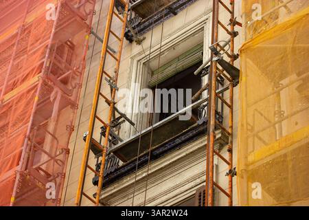 An einer Stadtfassade werden Baugerüste gezeigt, die während der Renovierung eines Gebäudes mit Sicherheitsnetz umwickelt sind. Das Äußere wird gerade renoviert Stockfoto